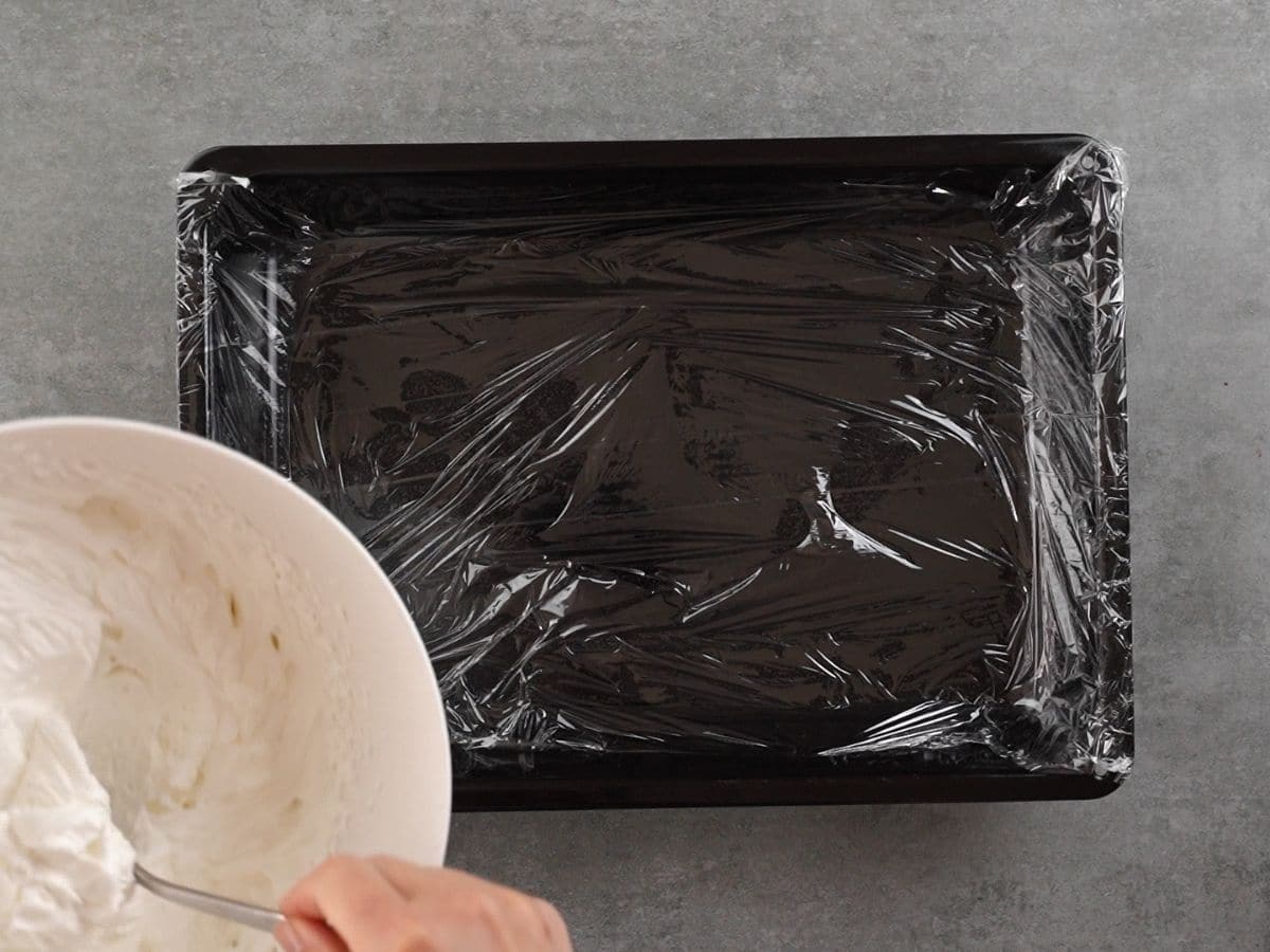 Placing plastic wrap into the bottom of a black baking dish