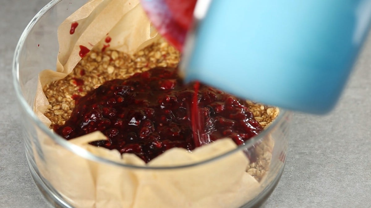 Pouring berry compote into round dish with granola base