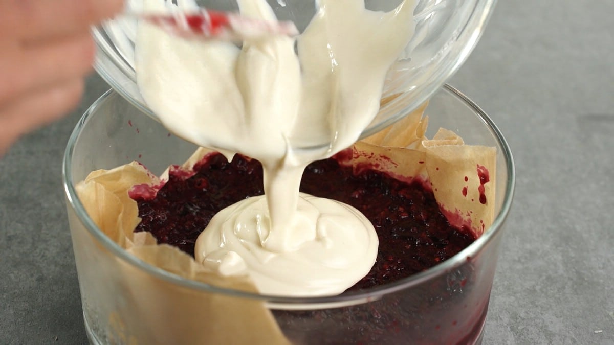 Hand pouring bowl of yogurt on top of berries in pan