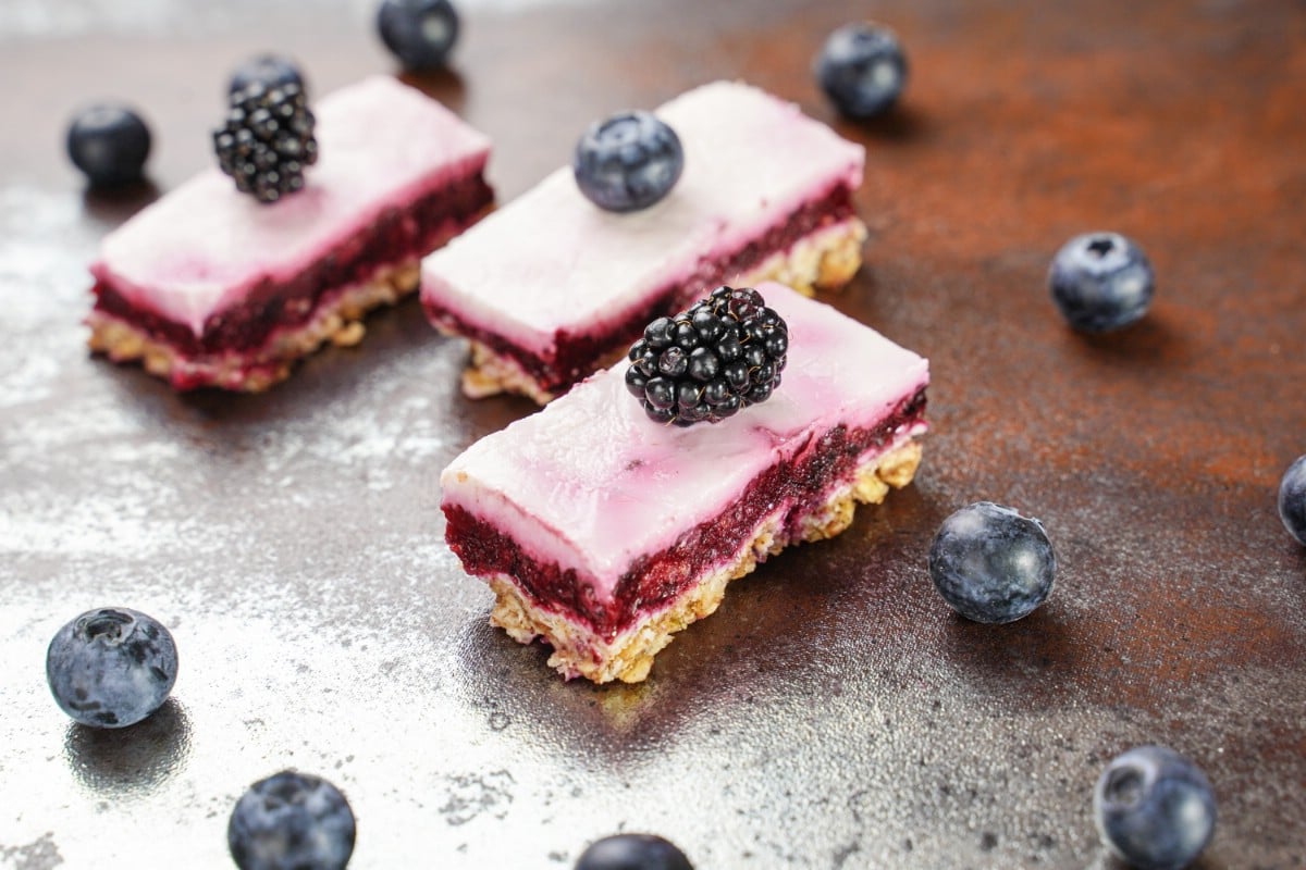 Frozen yogurt bars with three layers on table with blueberries and black berries on top