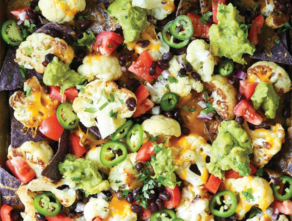 Cauliflower nachos topped with chilies, guacamole, chopped chives and parsley