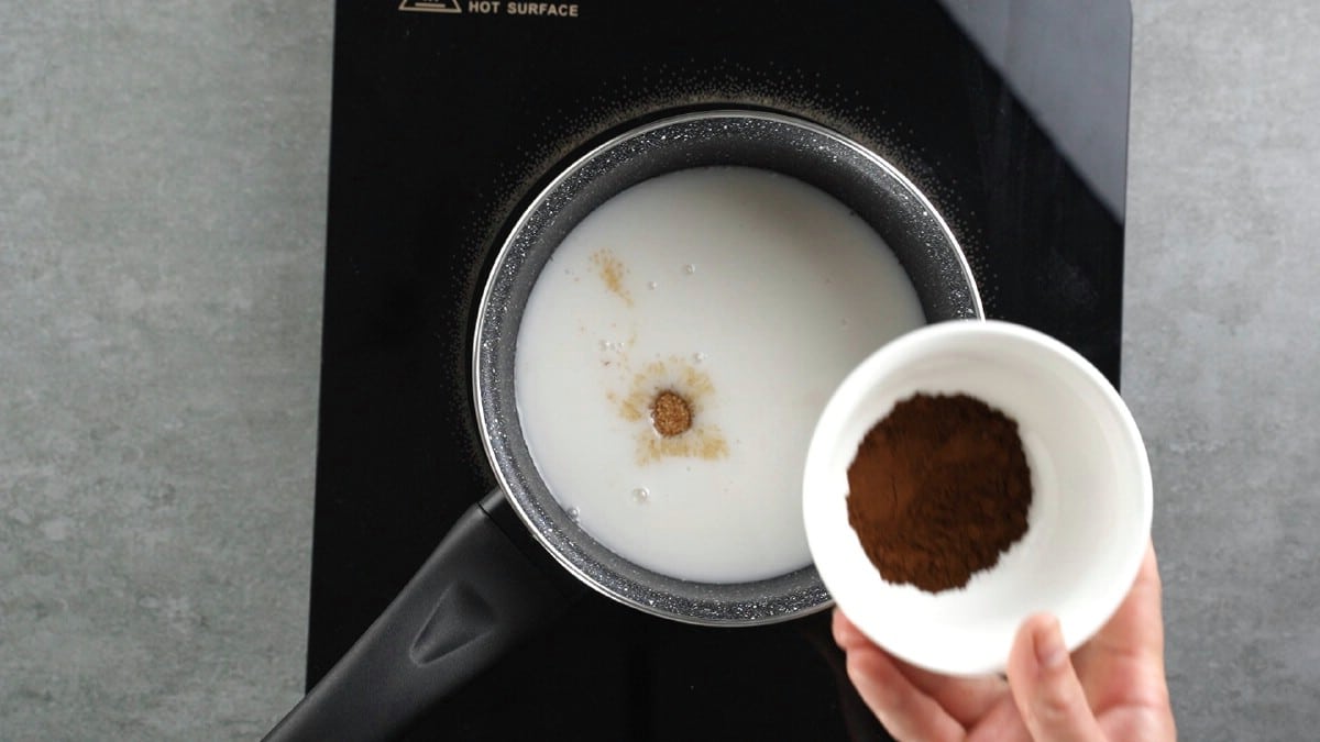Adding chocolate into milk in pan on stovetop