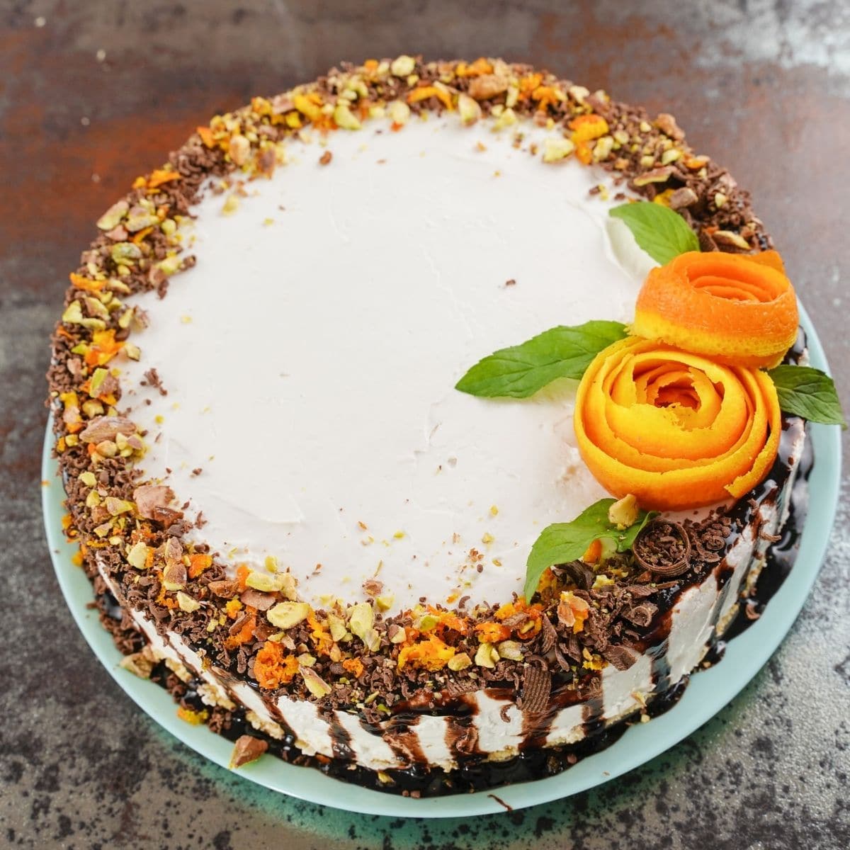 Cheesecake topped with chocolate syrup and orange roses on teal plate