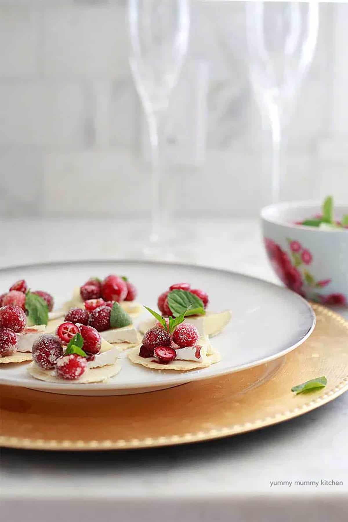crackers with cranberries, brie and topped with mint on a plate