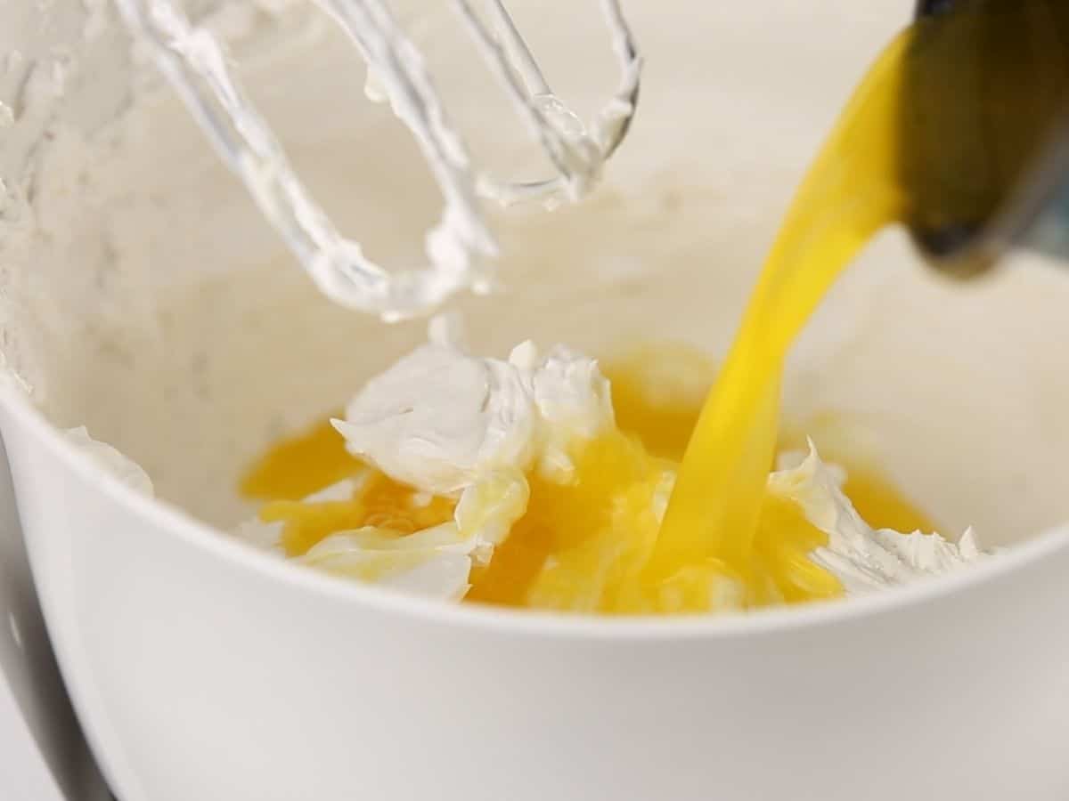 Pouring orange gelatin into cream cheese in white bowl
