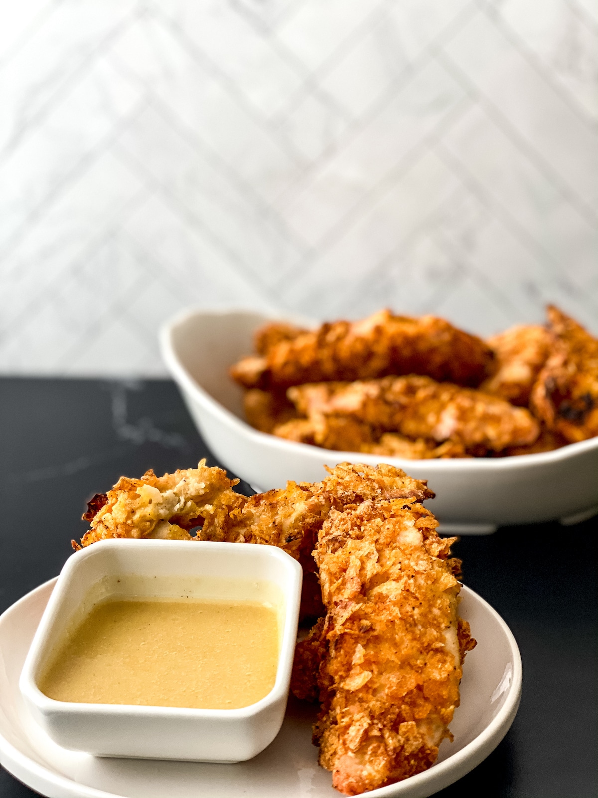 Chicken tenders in large white bowl in front of tile background