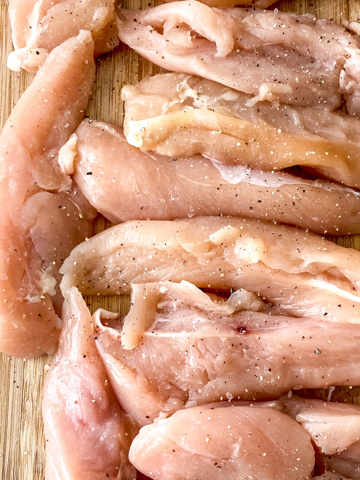 Seasoned raw chicken tenders on cutting board