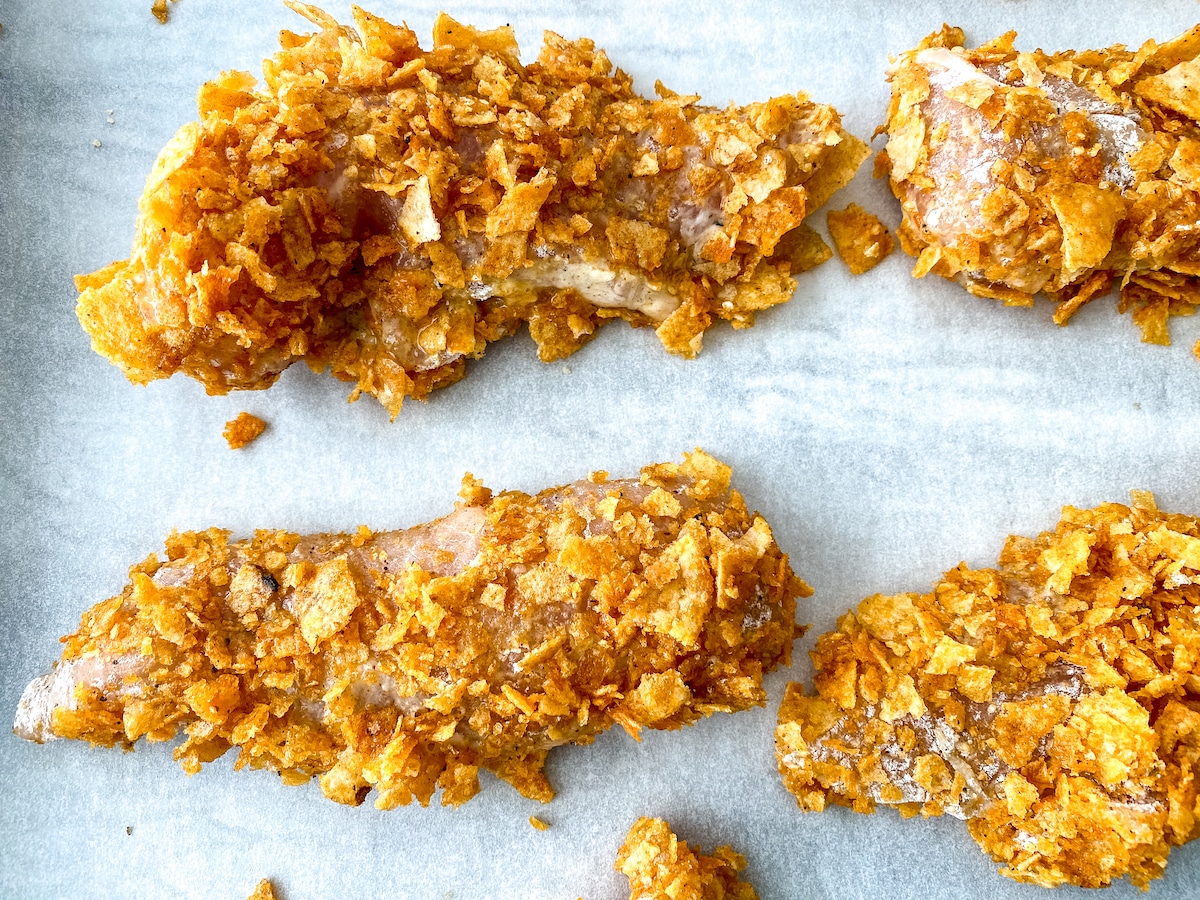 Chicken tenders coated in crunchy bits on baking sheet