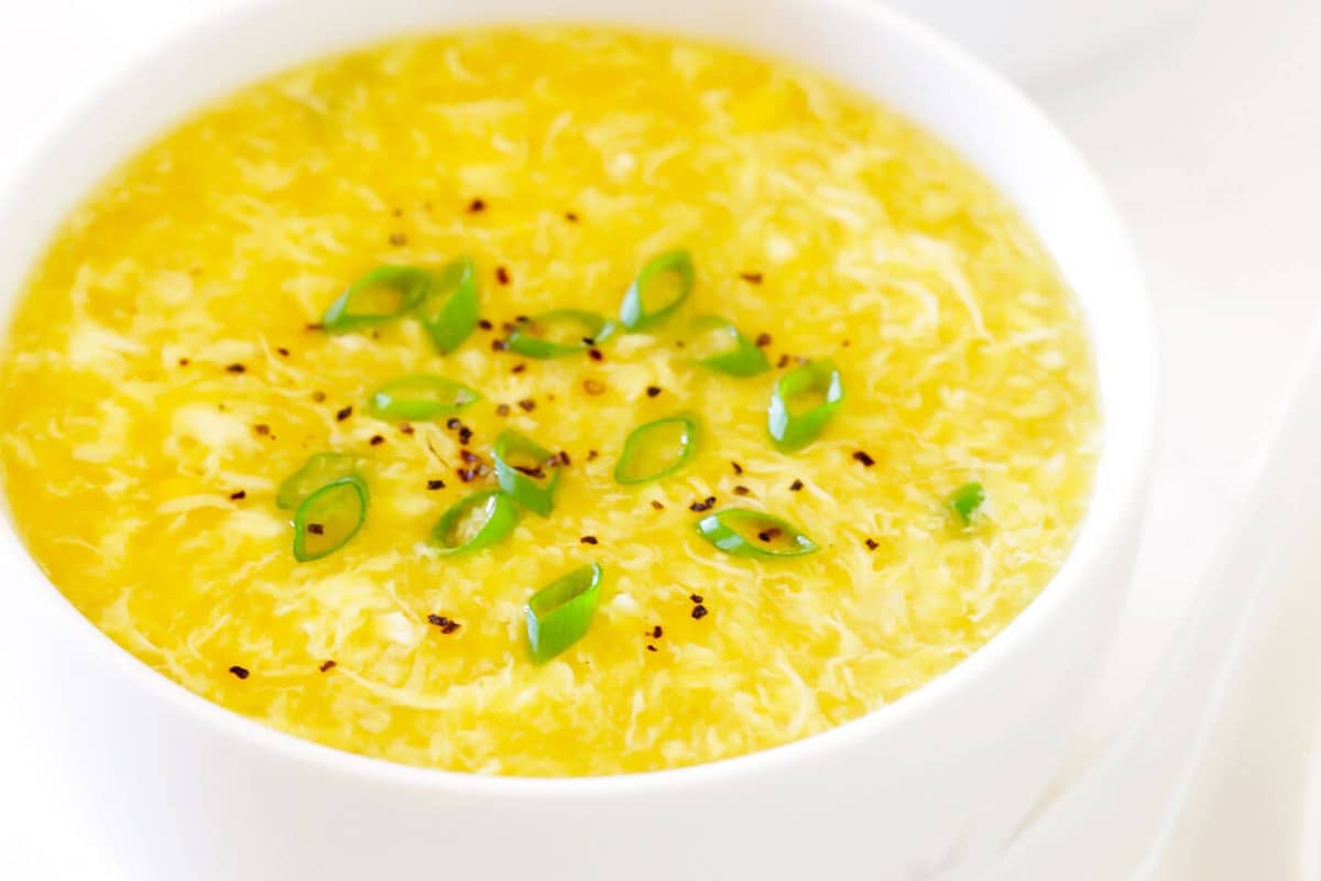 A bowl of egg drop soup topped with black peppermill and slices of onion leaves