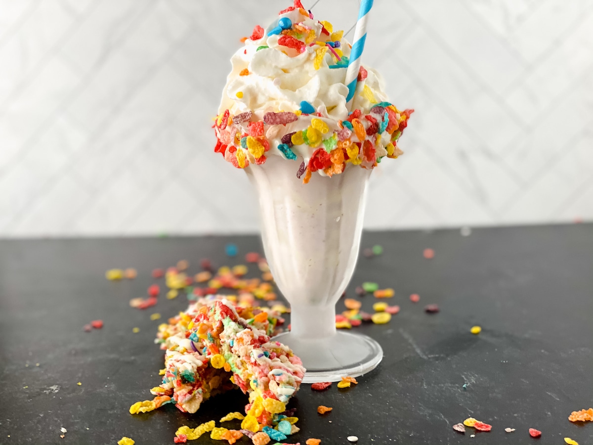 Milkshake in glass on black table with cereal pieces on table