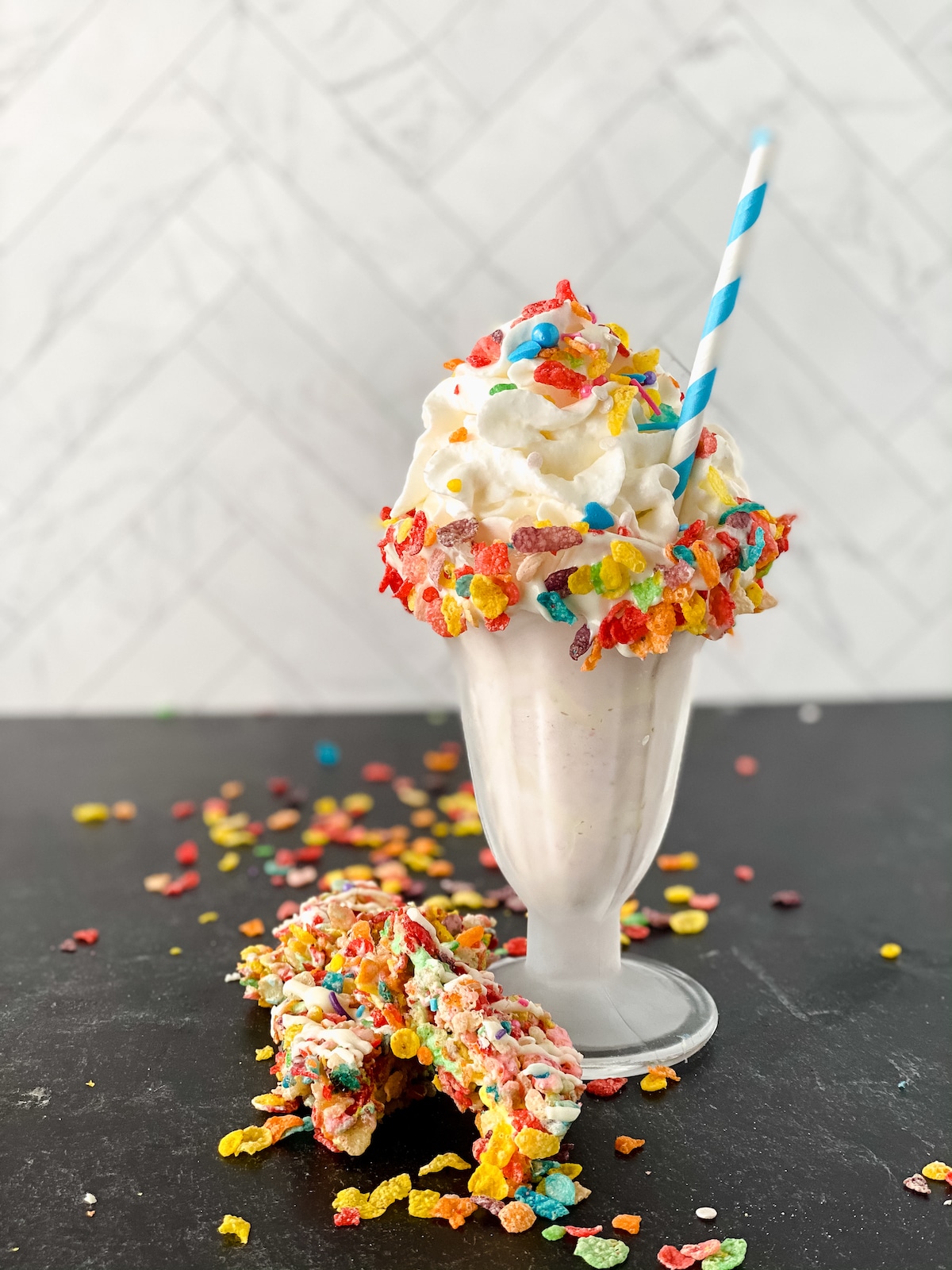Blue striped paper straw in top of milkshake topped with whipped cream and cereal