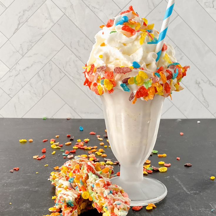 Old fashioned soda glass with milkshake topped with whipped cream and fruity pebbles on black table