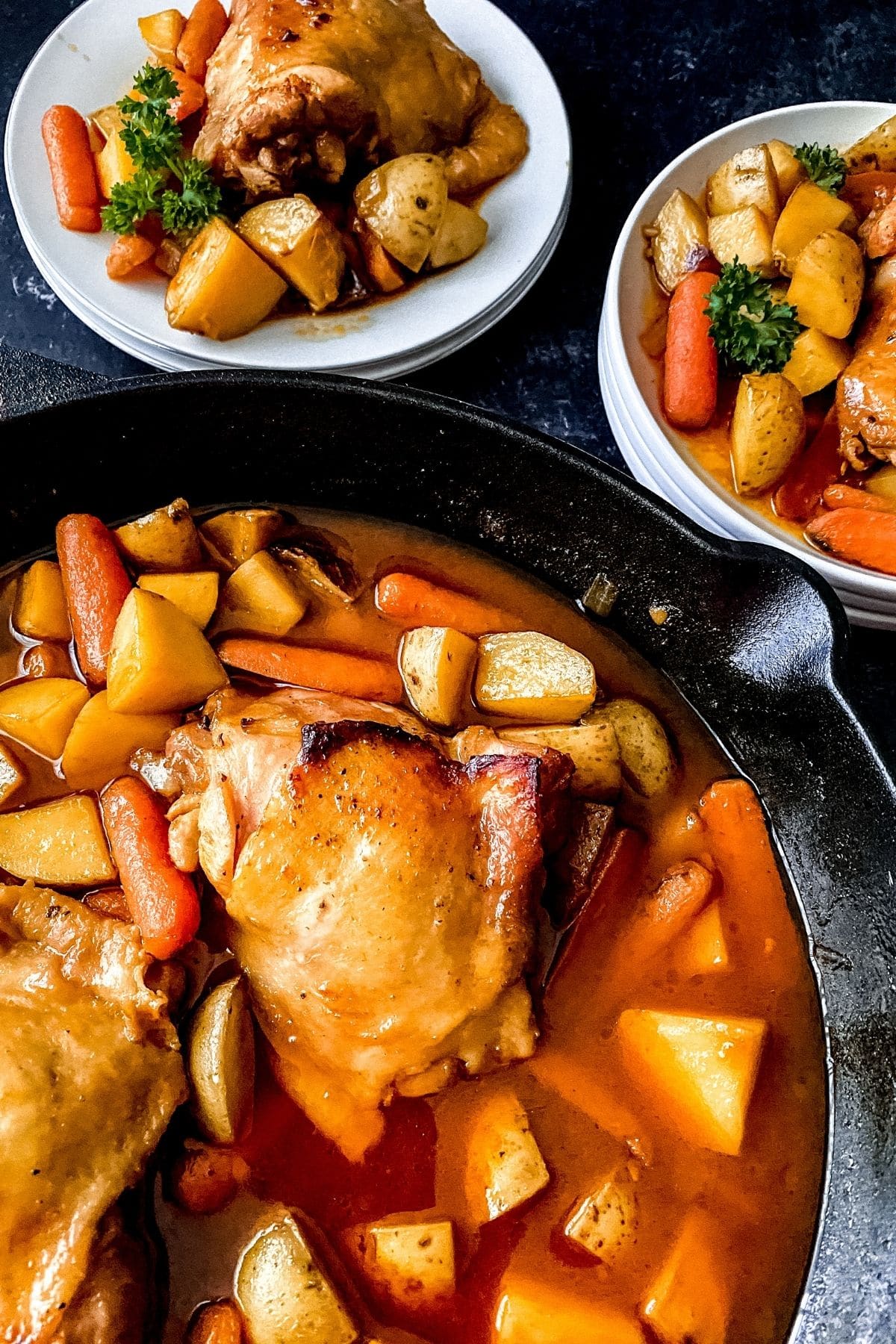 Skillet of chicken with vegetables in front of two white plates with same