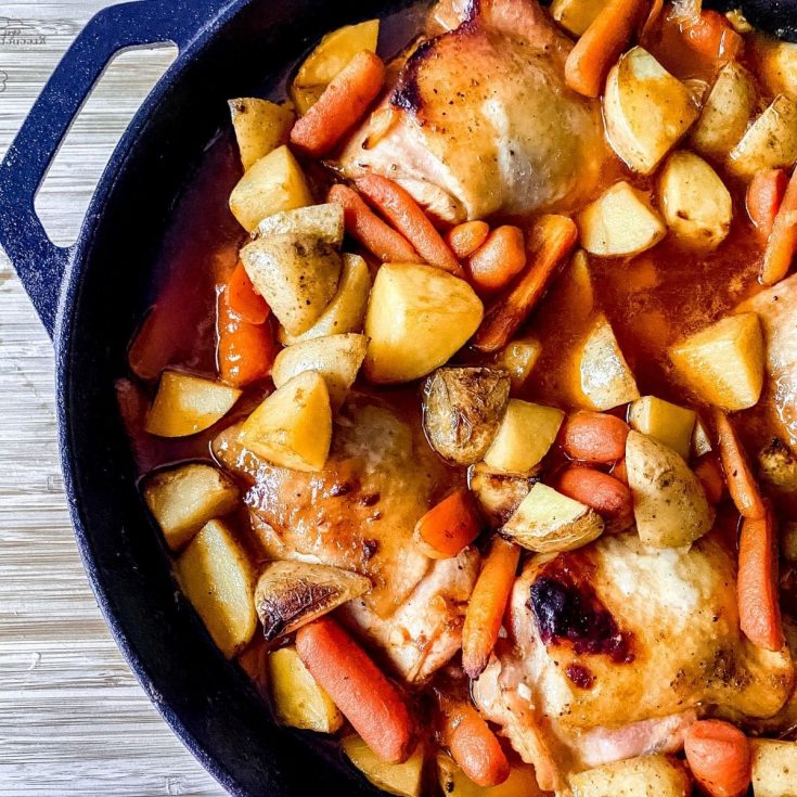 Cast iron skillet with chicken potatoes and carrots on gray table