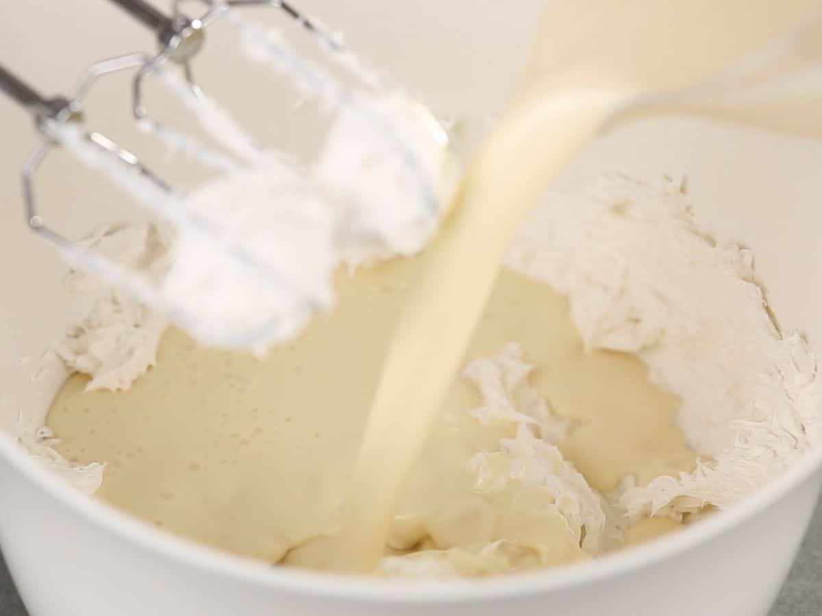 Pouring condensed milk into cream cheese in bowl