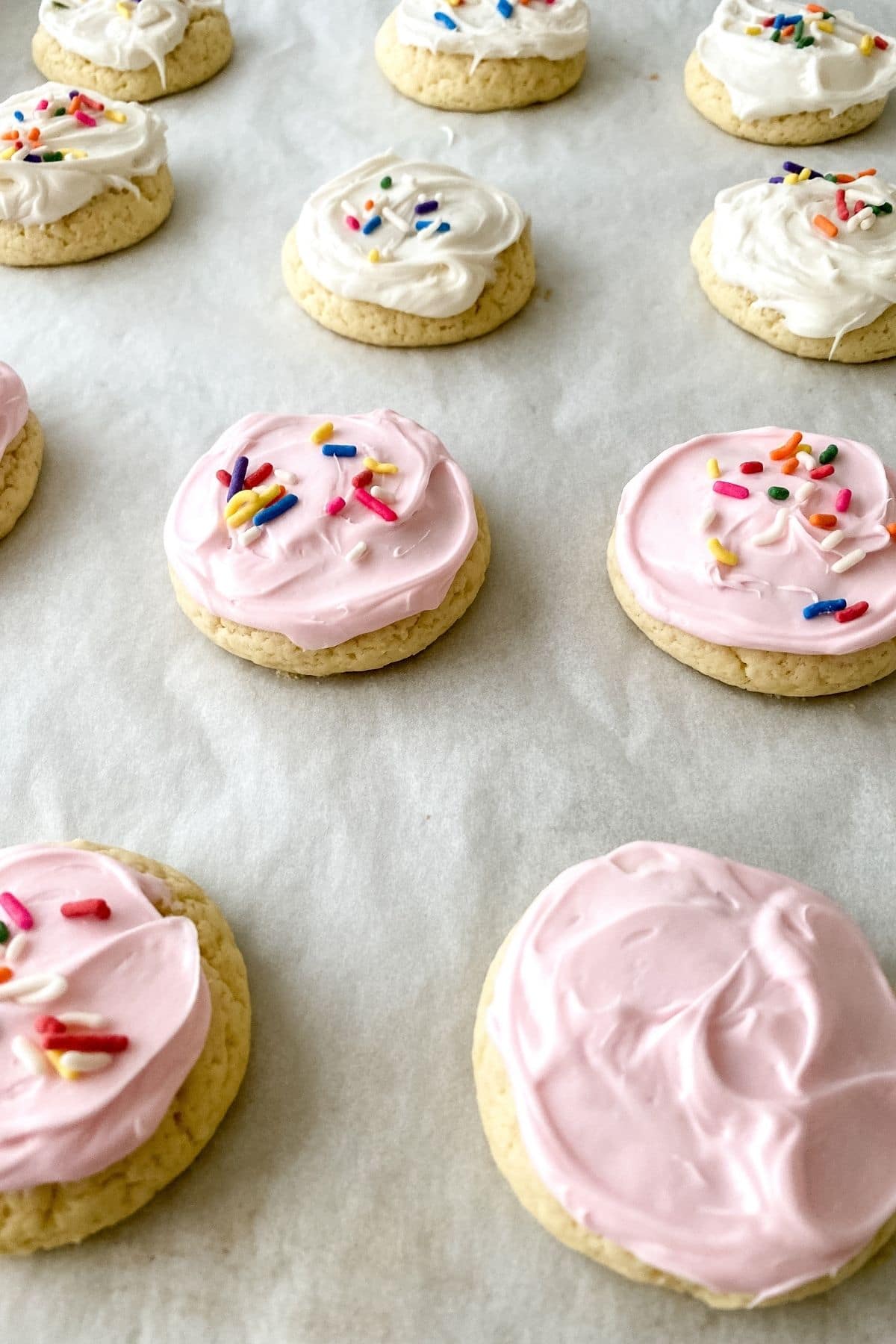 Light pink and white frosting on cookies laying on parchment paper