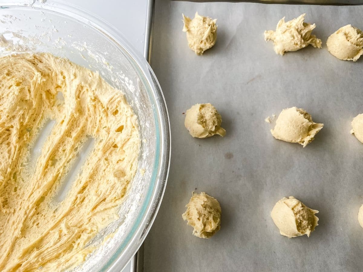 Bowl of dough by baking sheet with scoops of cookie dough