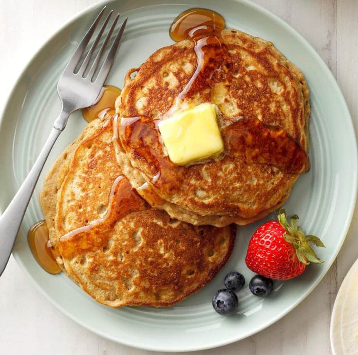 Oatmeal Pancakes topped with butter and maple syrup and fruits on the side