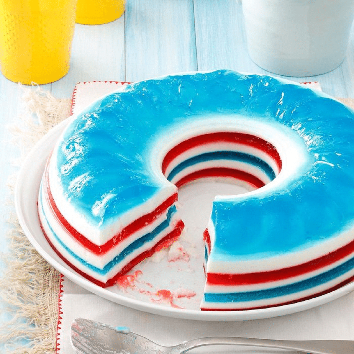 Layered red white and blue gelatin ring with slice cut out on white plate by spoon