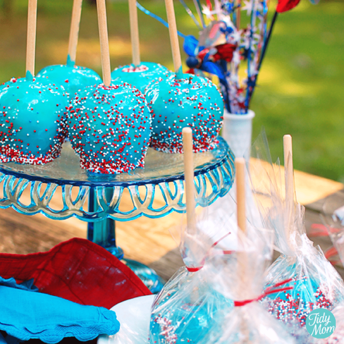 Apples dipped in blue coating with red white and blue sprinkles on tall blue cake stand