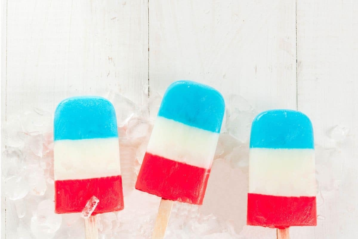 Three red white and blue layered popsicles in ice on white table