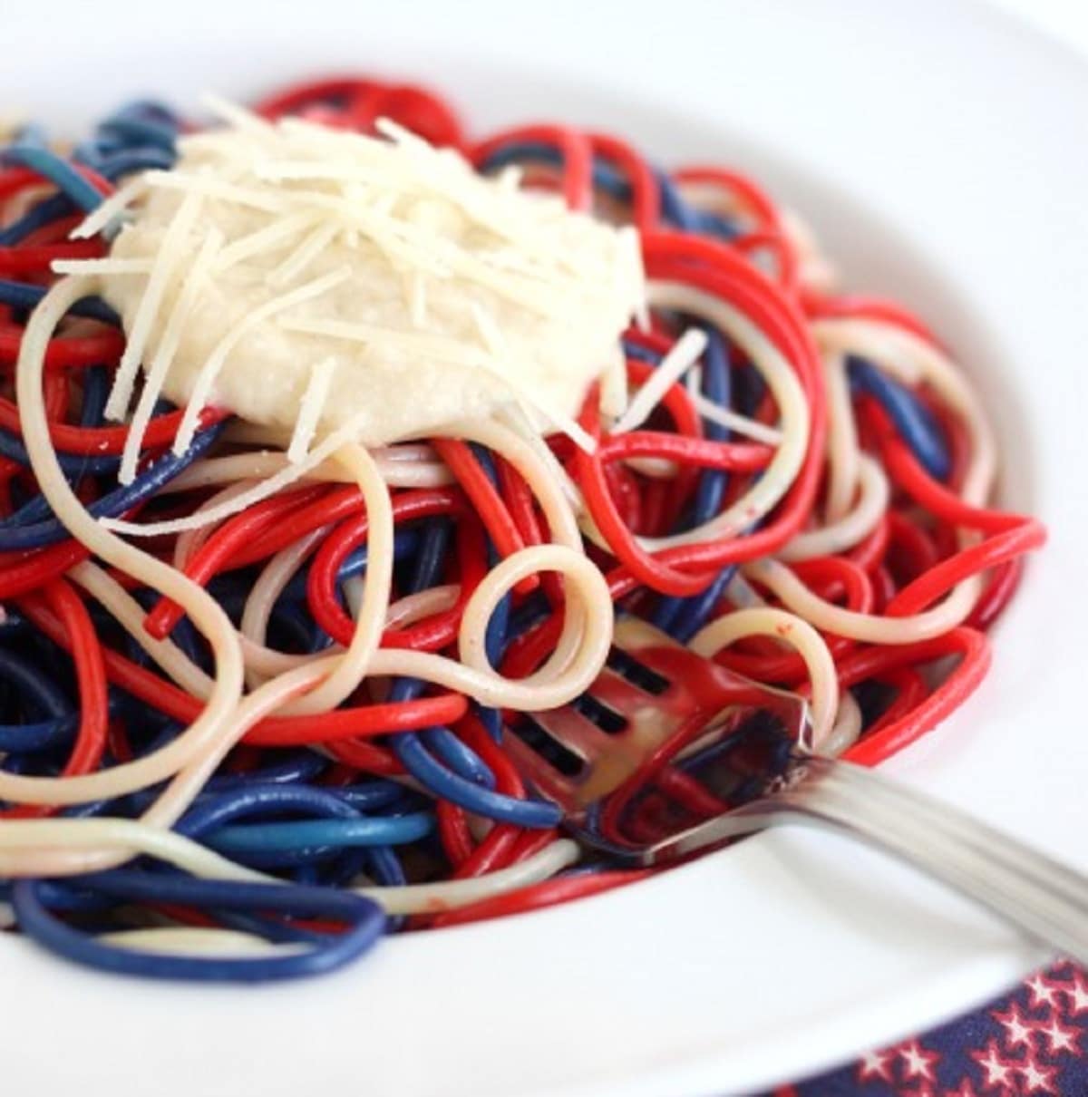 Noodles dyed red and blue topped with dollop of cheese in white bowl