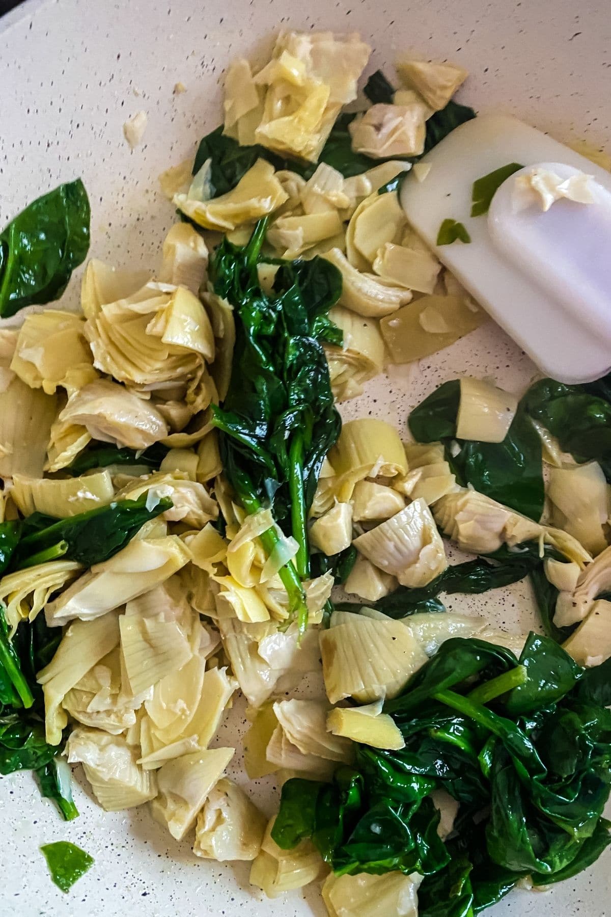 Spinach with artichoke hearts in skillet with white spatula