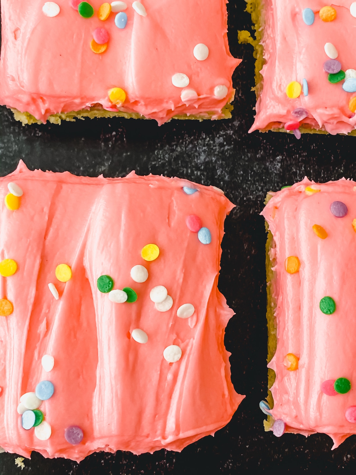 Pink frosted cake bar with sprinkles on black table