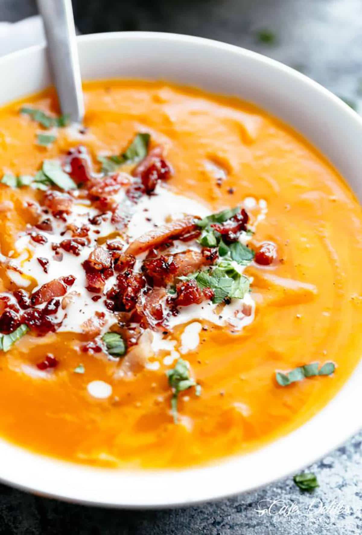 Thick & Creamy Pumpkin Soup served with a swirl of cream, crispy bacon pieces and on the side cheesy garlic bread.