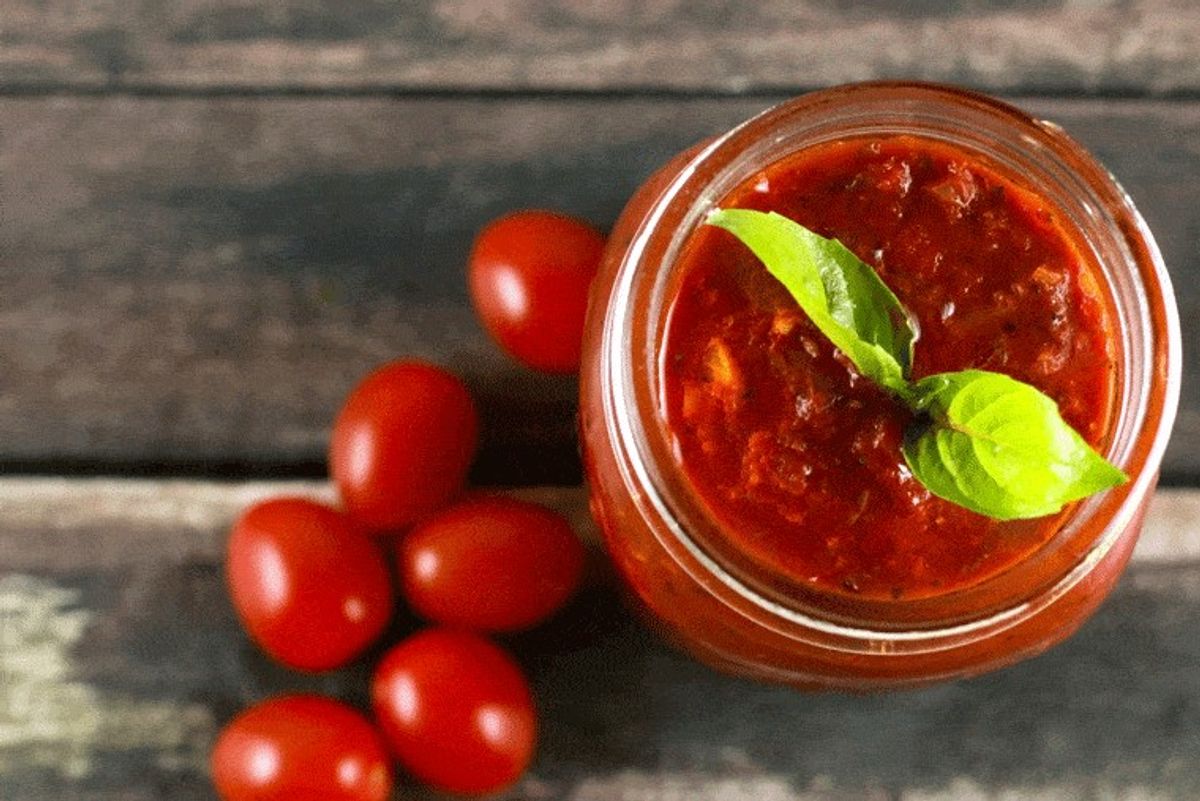 mason jar of pasta sauce on wood table next to cherry tomatoes