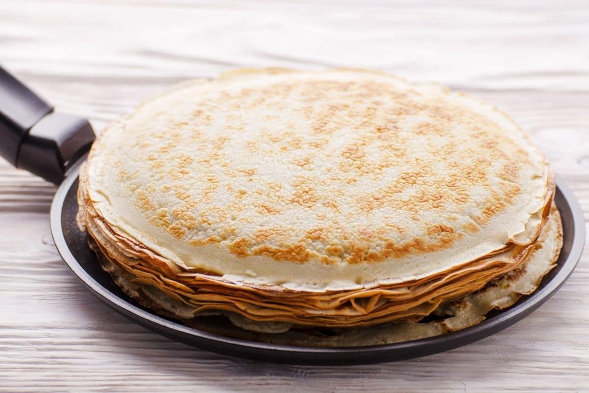 Stack of French crepes in crepe pan on wooden kitchen table