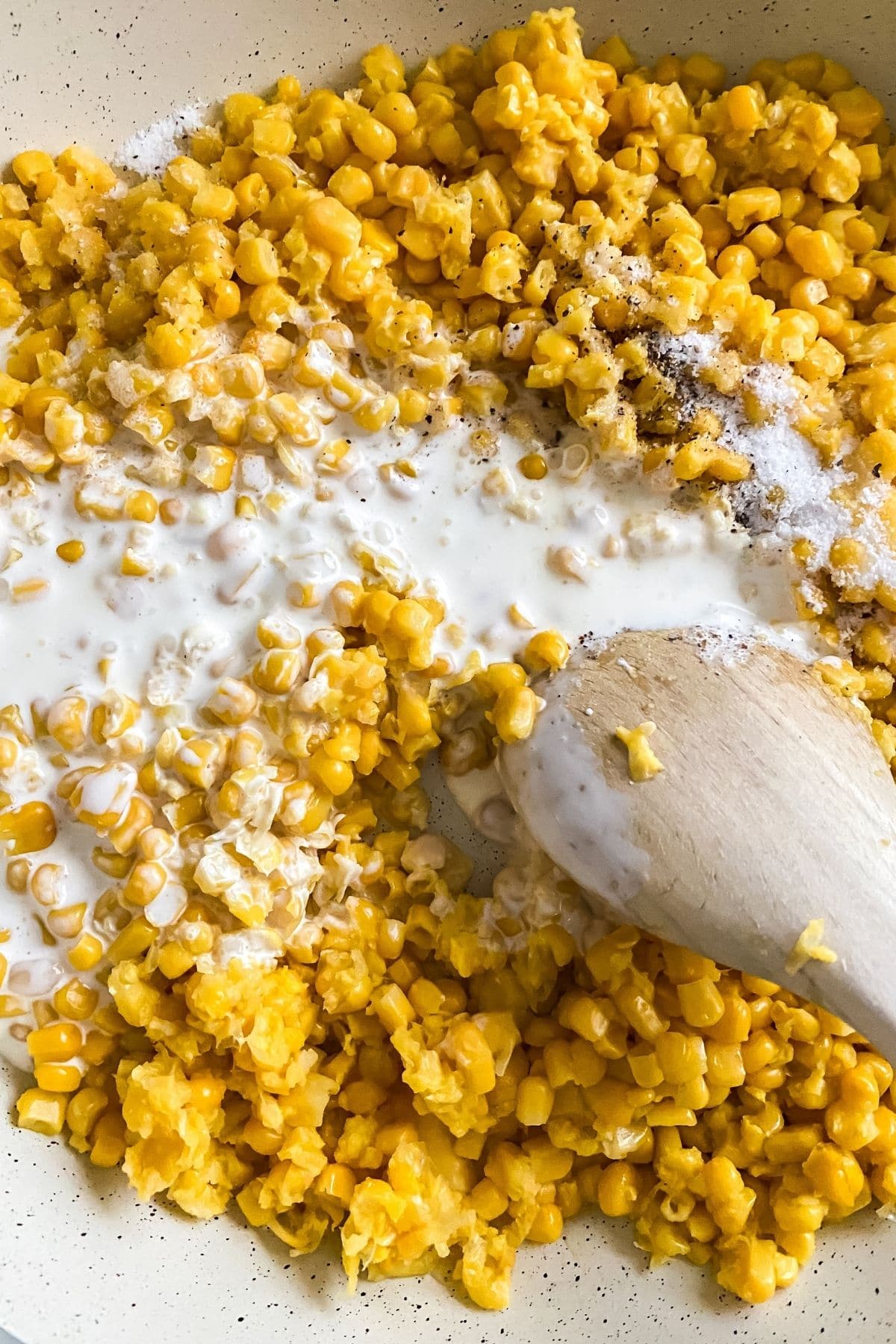 Corn and cream in skillet with wooden spoon