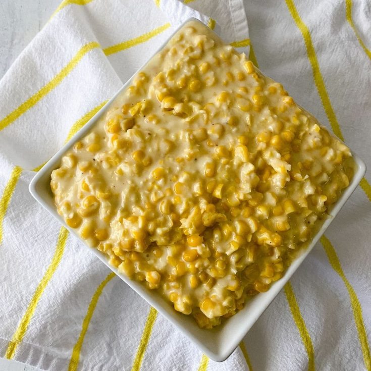 Creamed corn in square white bowl sitting on white and yellow napkin