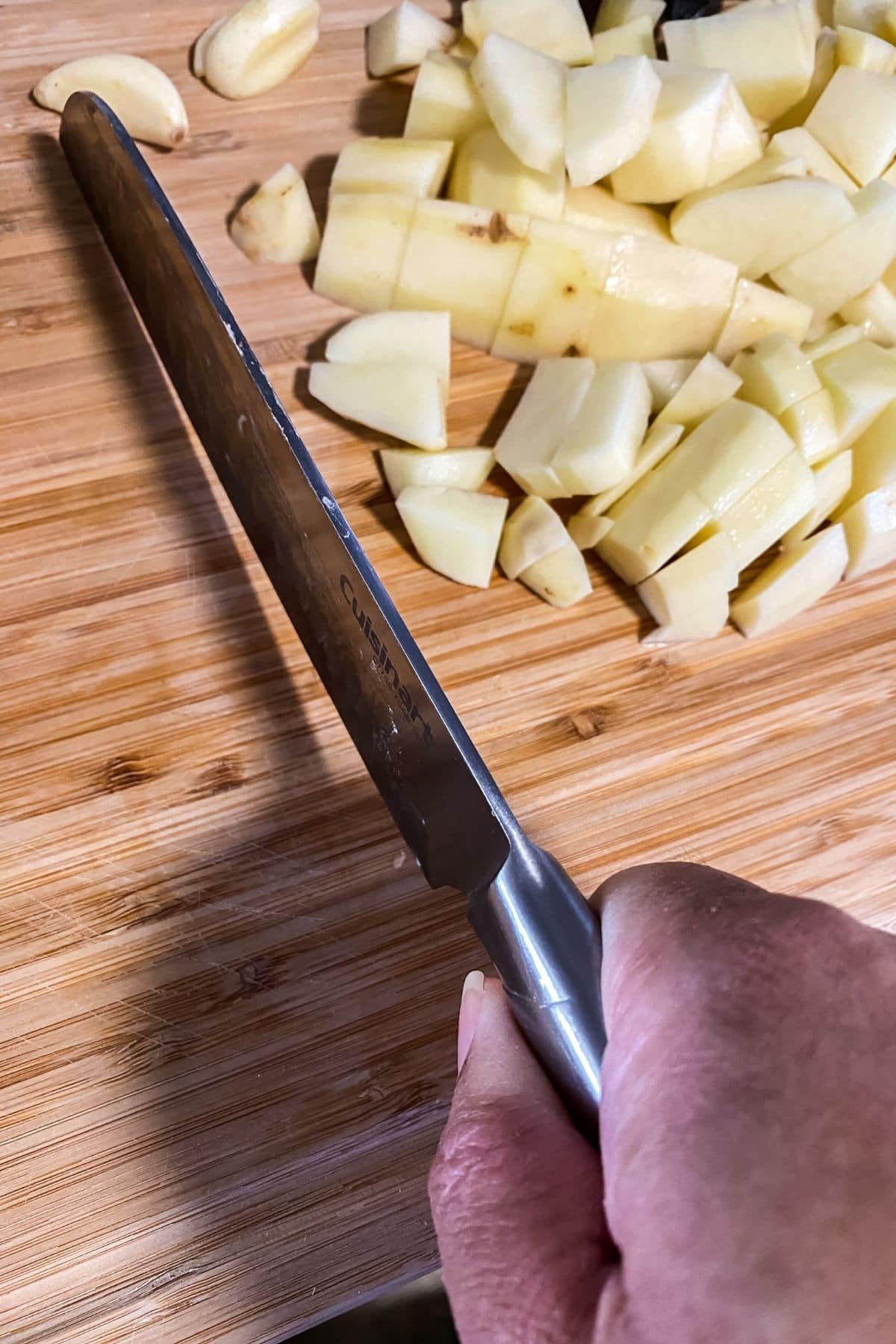 Hand holding knife cutting potatoes on wooden board