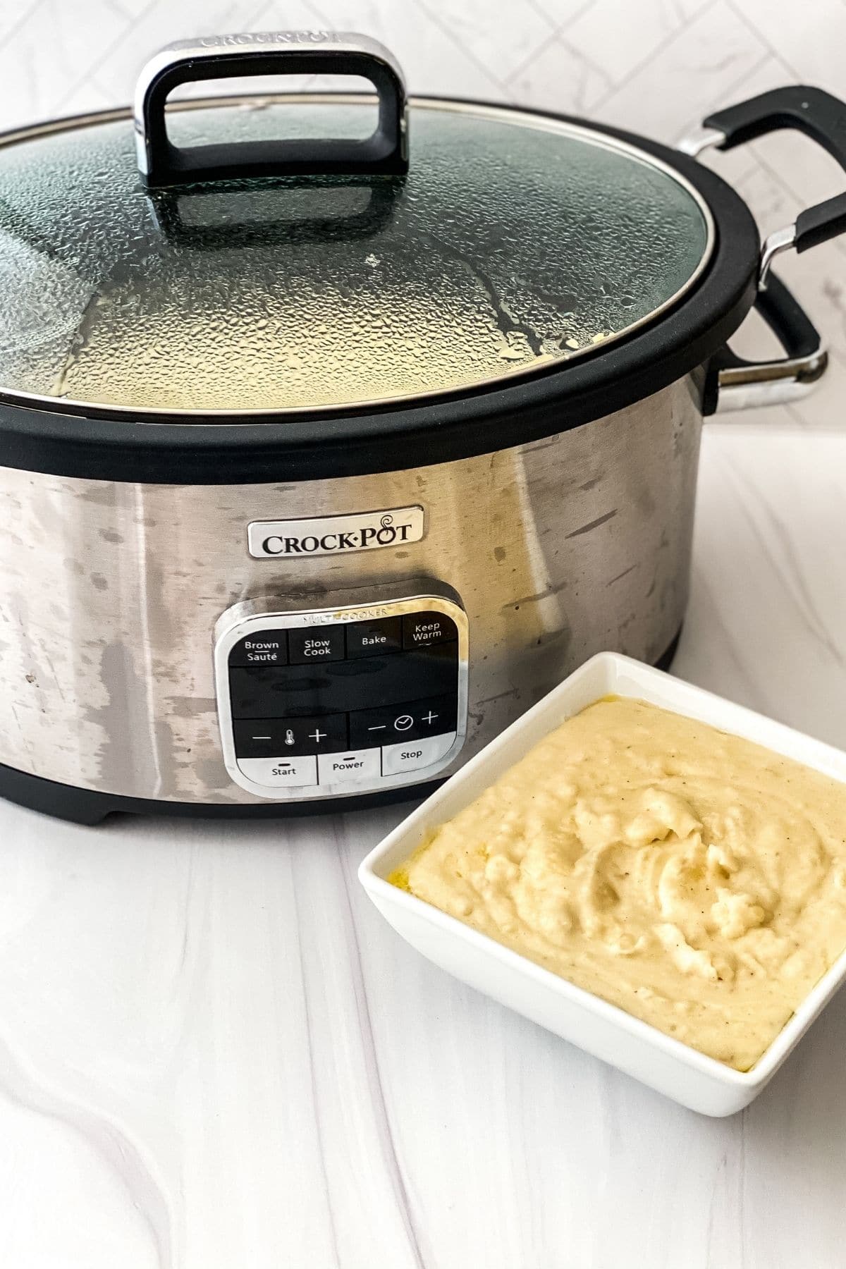 Crockpot with lid on by white bowl of mashed potatoes