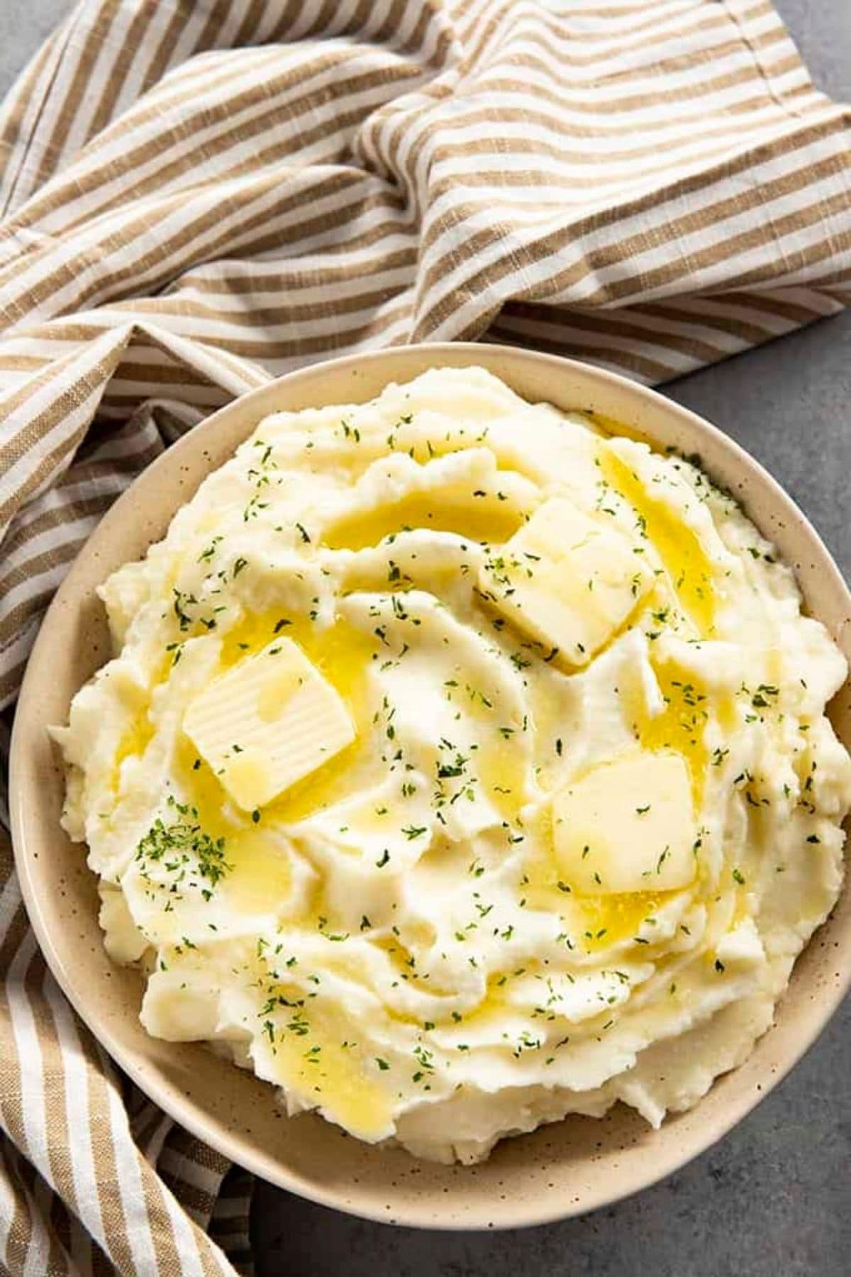 Large brown bowl of mashed potatoes with pats of butter on top
