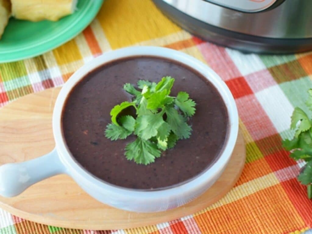 White soup mug of black bean soup on plaid tablecloth