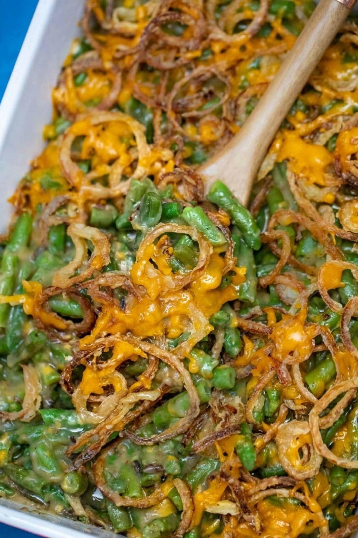 wooden spoon in casserole dish of green beans with onions on top