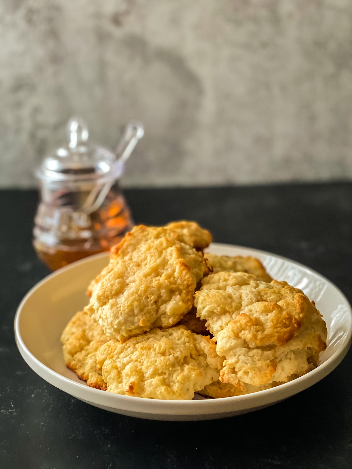 Honey butter biscuits on white bowl sitting on table with glass jar of honey in background