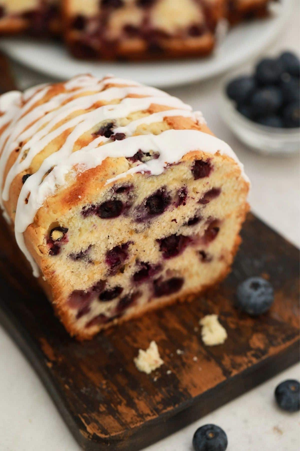 blueberry bread with drizzle of glaze on top sitting on wood cutting board