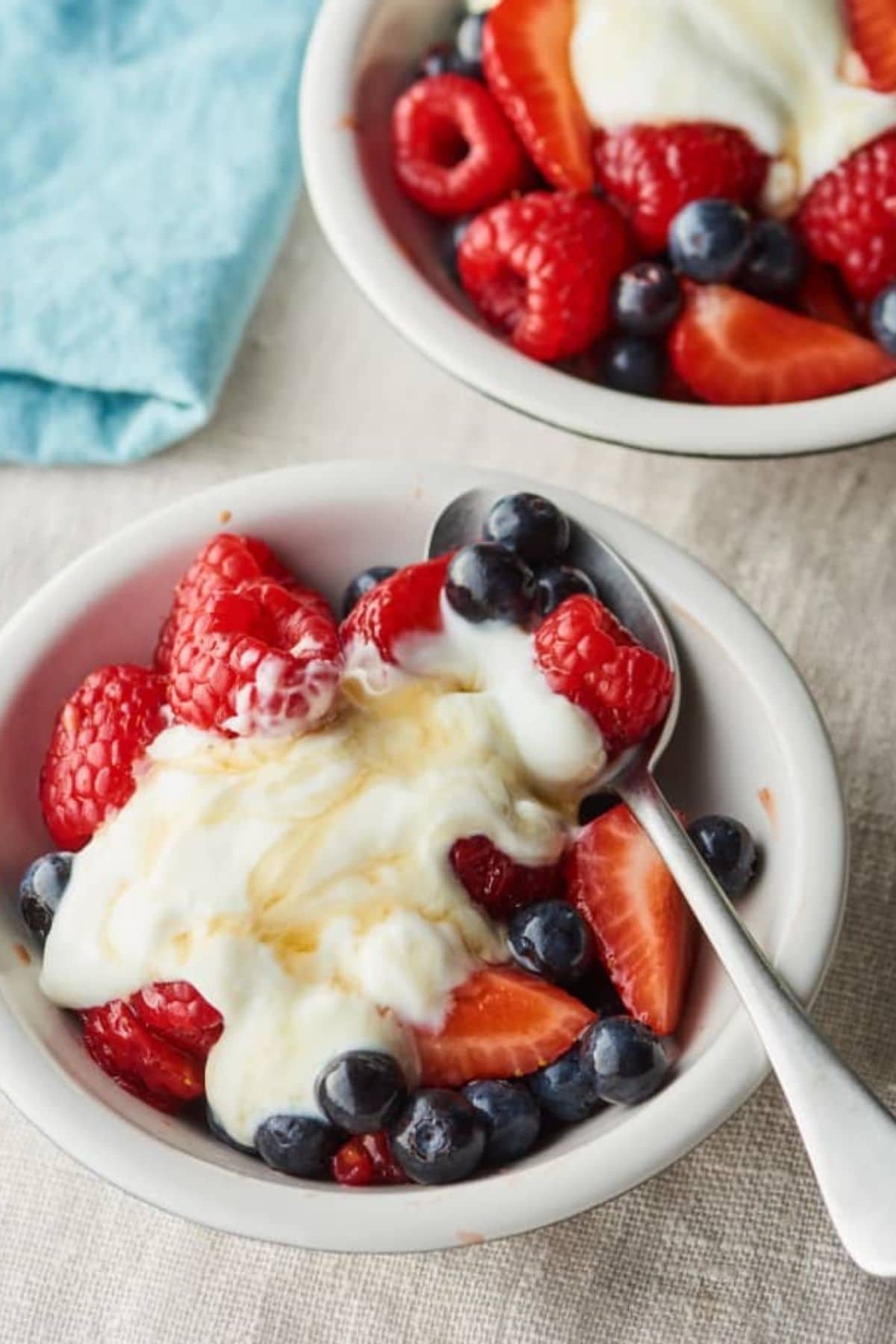 Small white bowl of mixed berries and yogurt by blue napkin