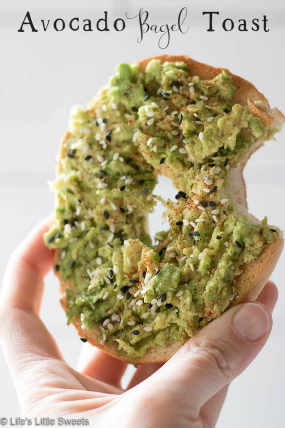 Hand holding half a bagel with avocado spread