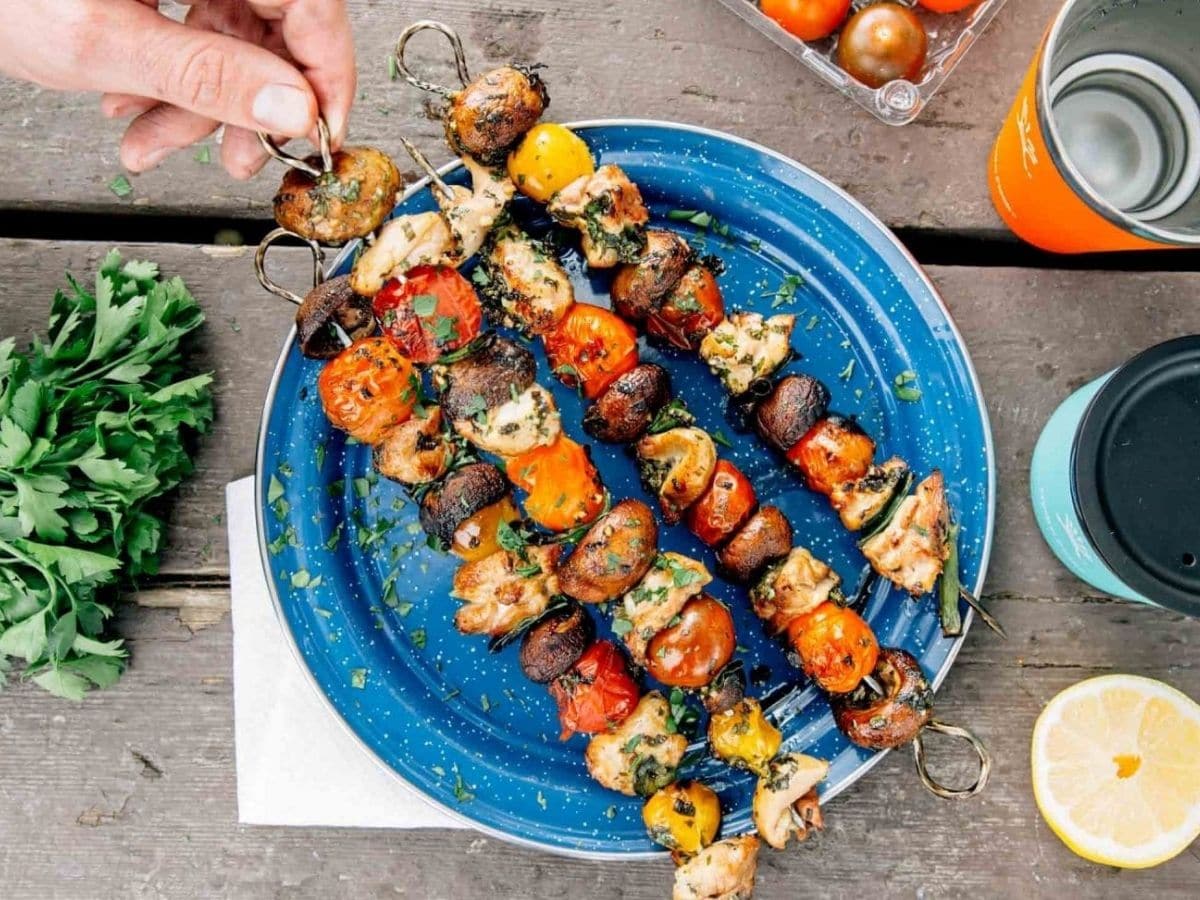 Chicken kebabs with vegetables on blue plate sitting on wood table