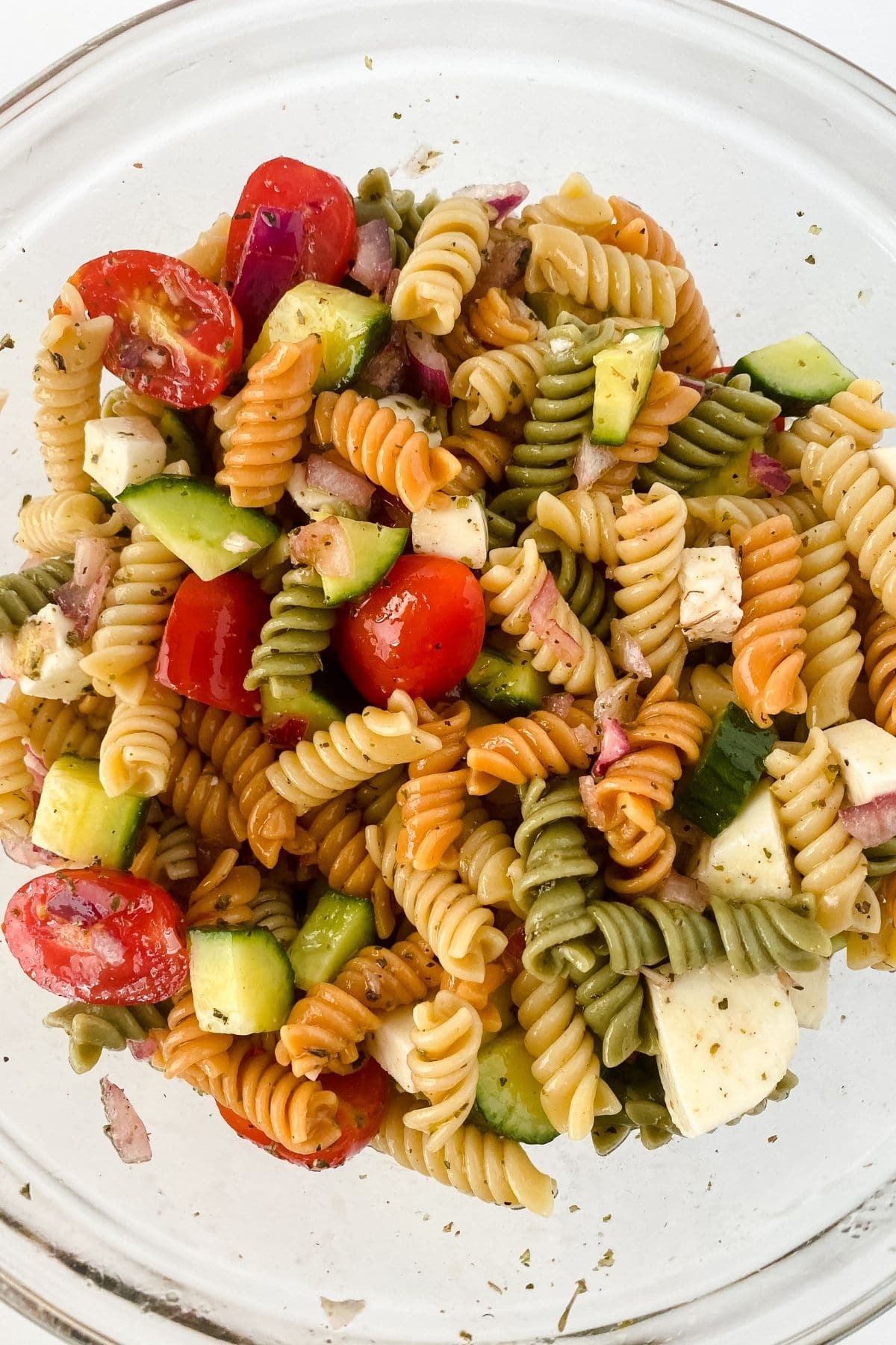 Large glass bowl of rotini pasta salad with cherry tomatoes and cucumbers