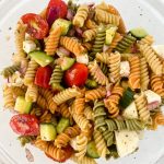 Glass bowl of rotini pasta with cheese cucumbers and tomato