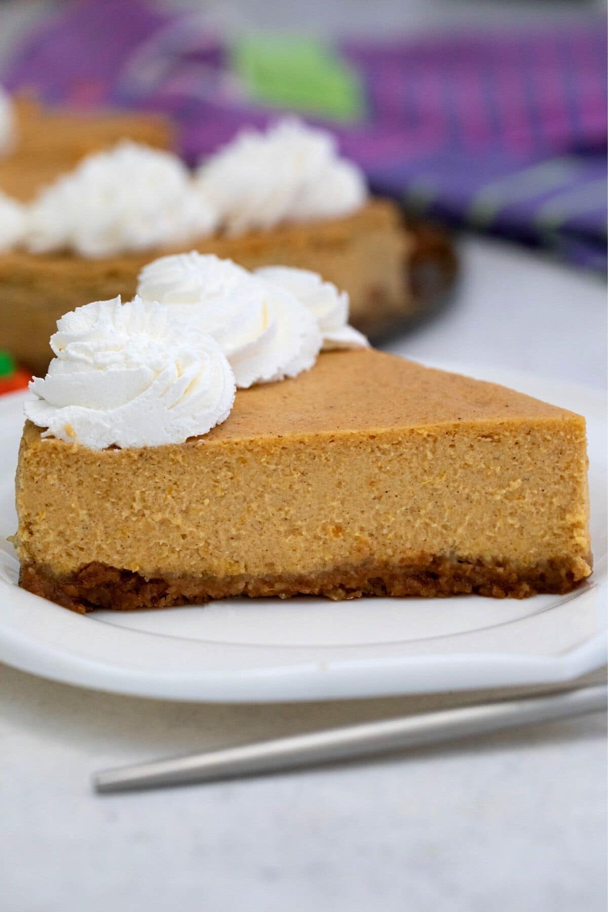 Side slice of pumpkin cheesecake on white plate by fork