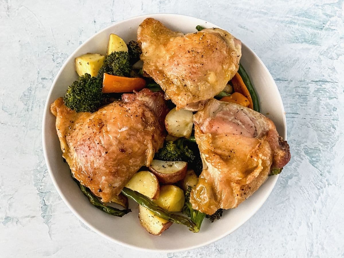 Chicken thighs and vegetables in white bowl on marble table