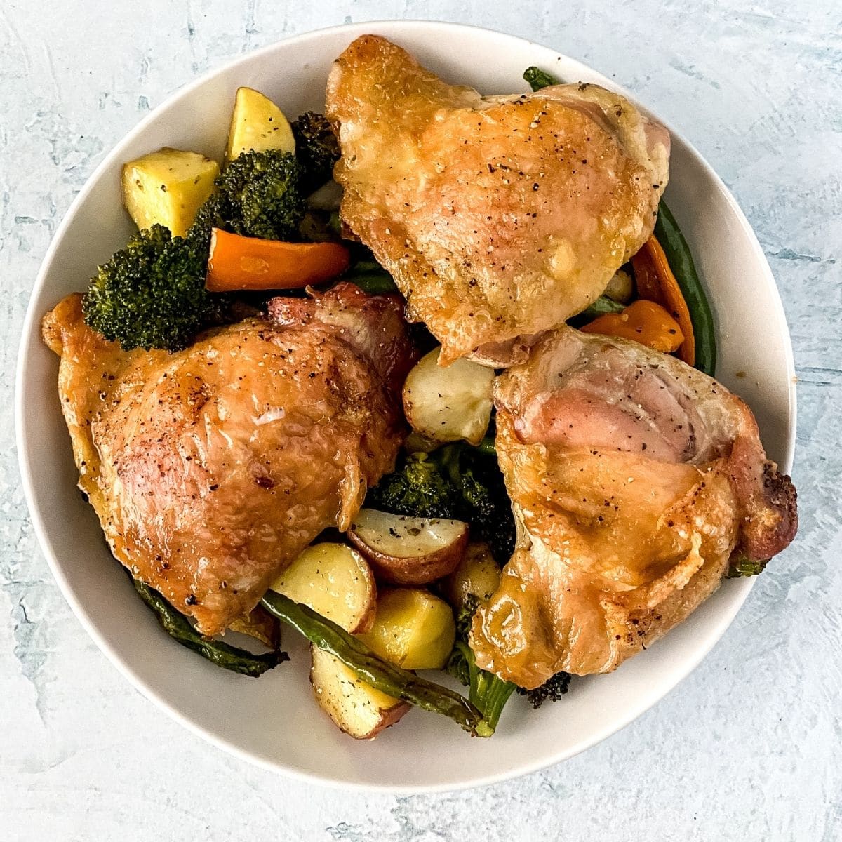 White bowl of chicken thighs and vegetables