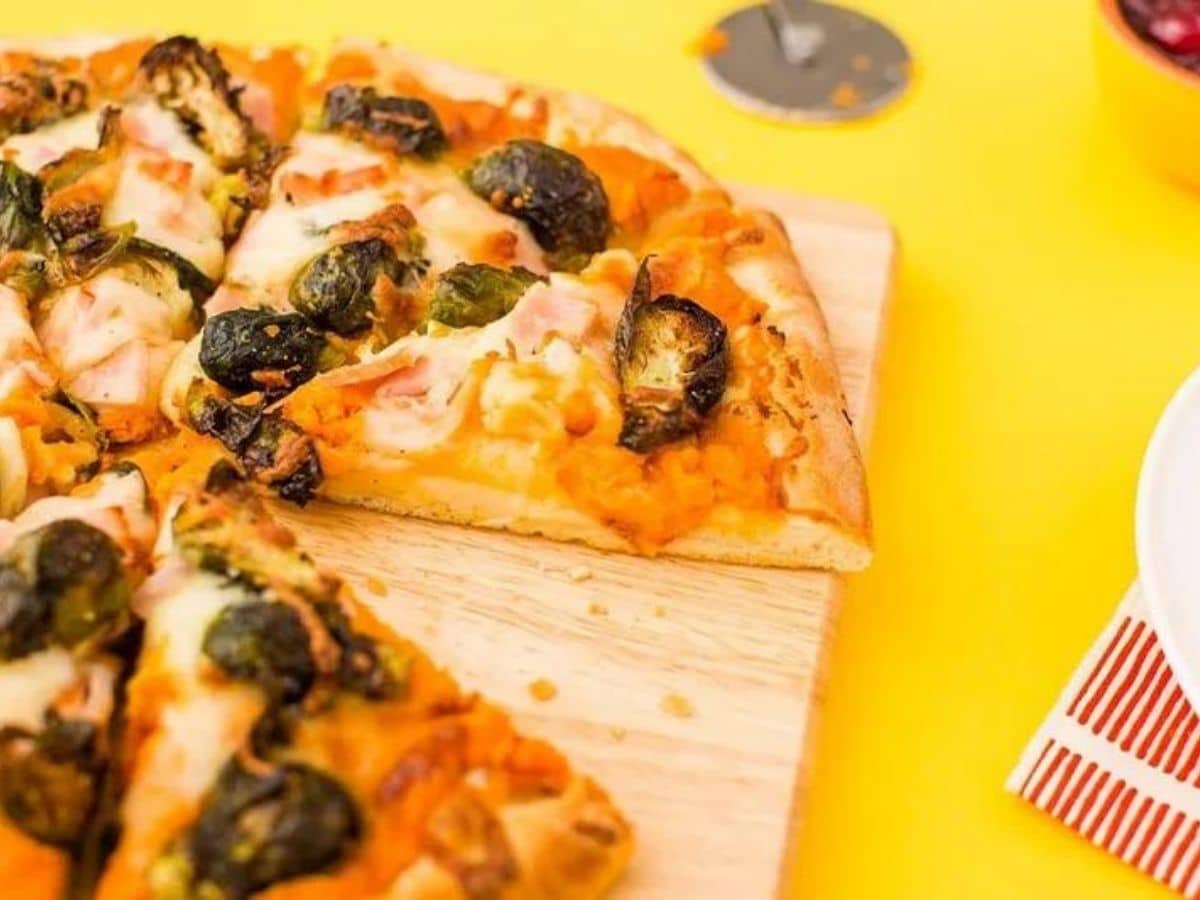 pizza with brussels sprouts on wood platter sitting on yellow tablecloth