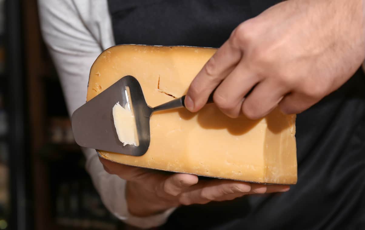 Young chef slicing aged cheese with a cheese slicer.